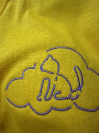 a close up of a yellow t - shirt with a purple logo on it